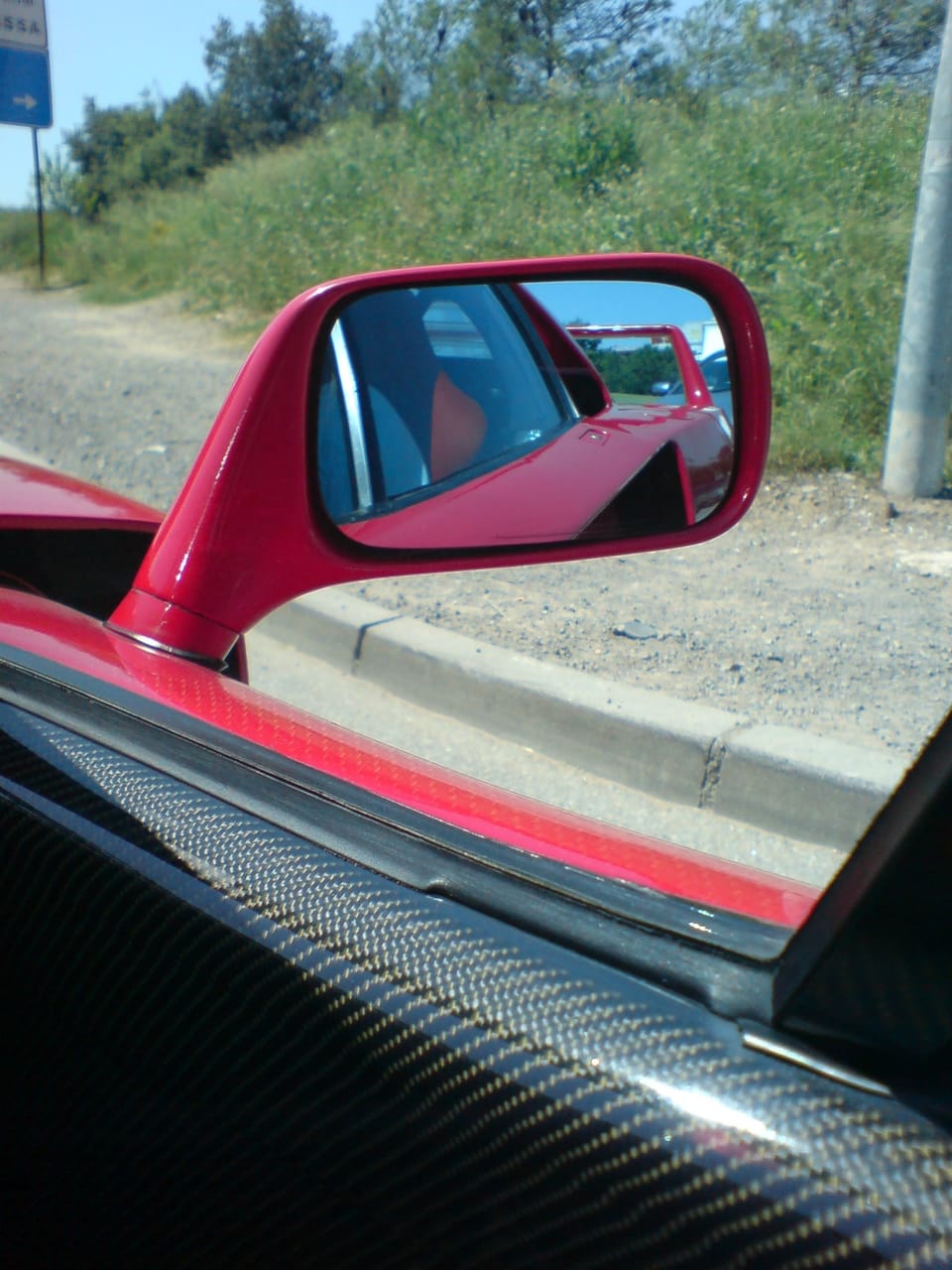 Side mirror of a red Ferrari F40 reflecting the rear wing
